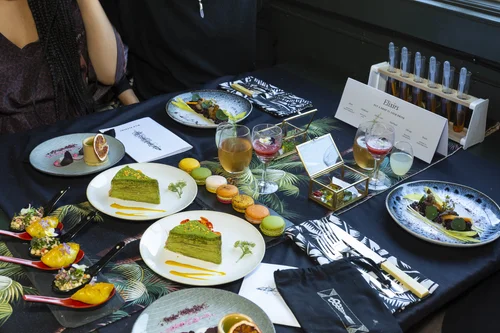 A dining table laid with matcha cake, canapés, elixirs in test tubes and botanical linens